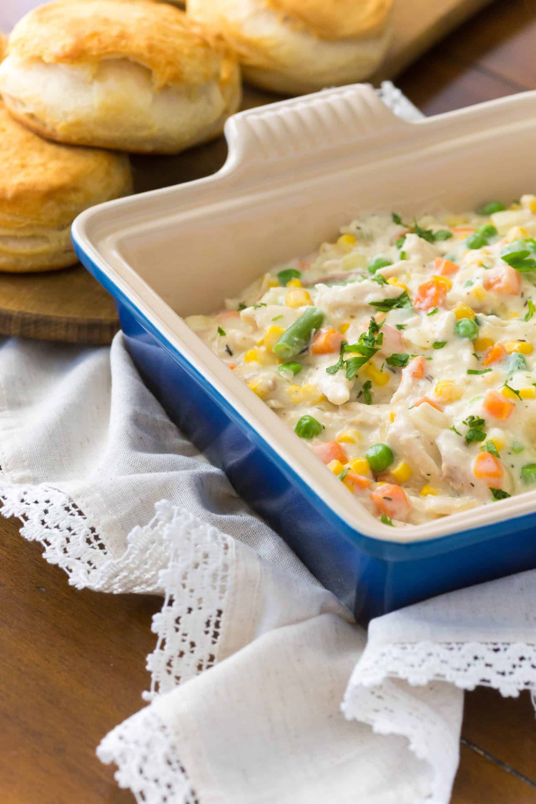 A container of chicken pot pie filling is served next to biscuits.