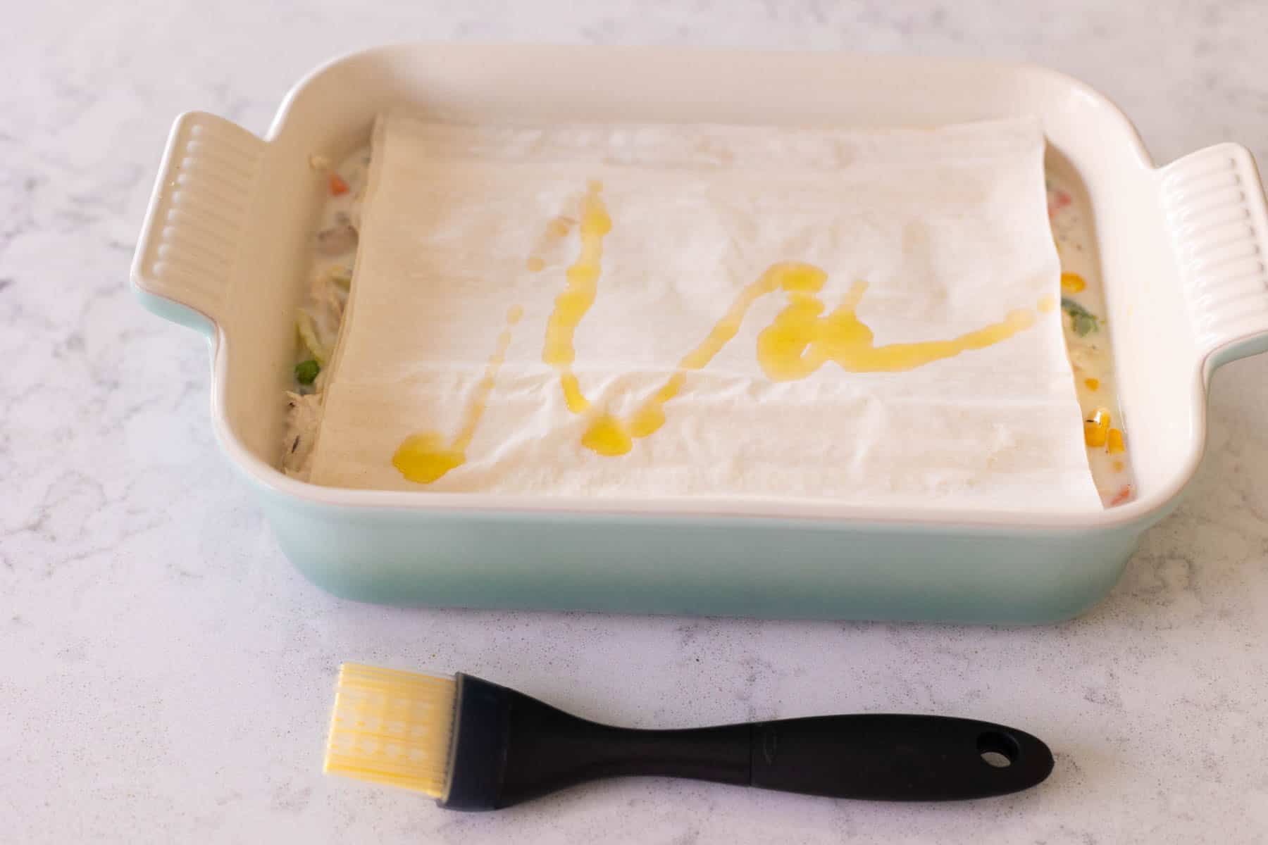 The sheets of phyllo dough have been placed on top of the baking dish and drizzled with olive oil.