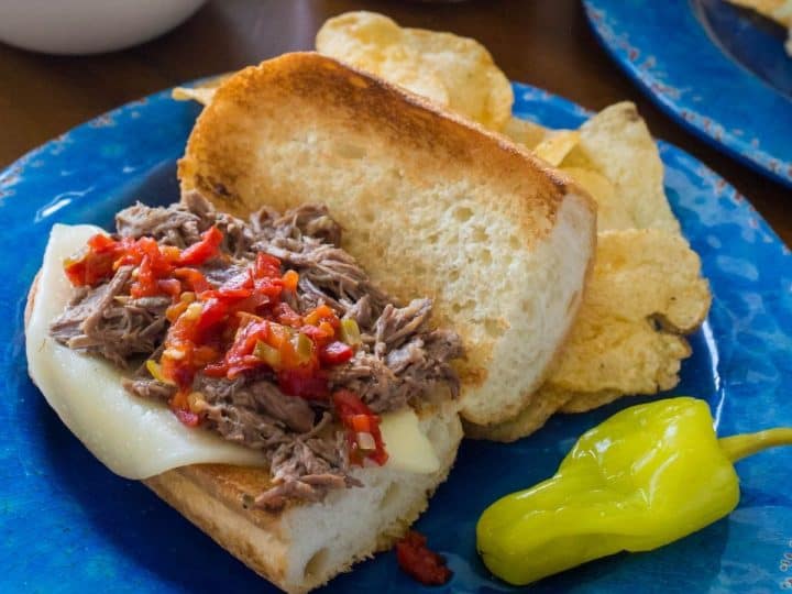Italian beef sandwich has toasted bread, melted provolone cheese, and pepper relish on top of the shredded beef.