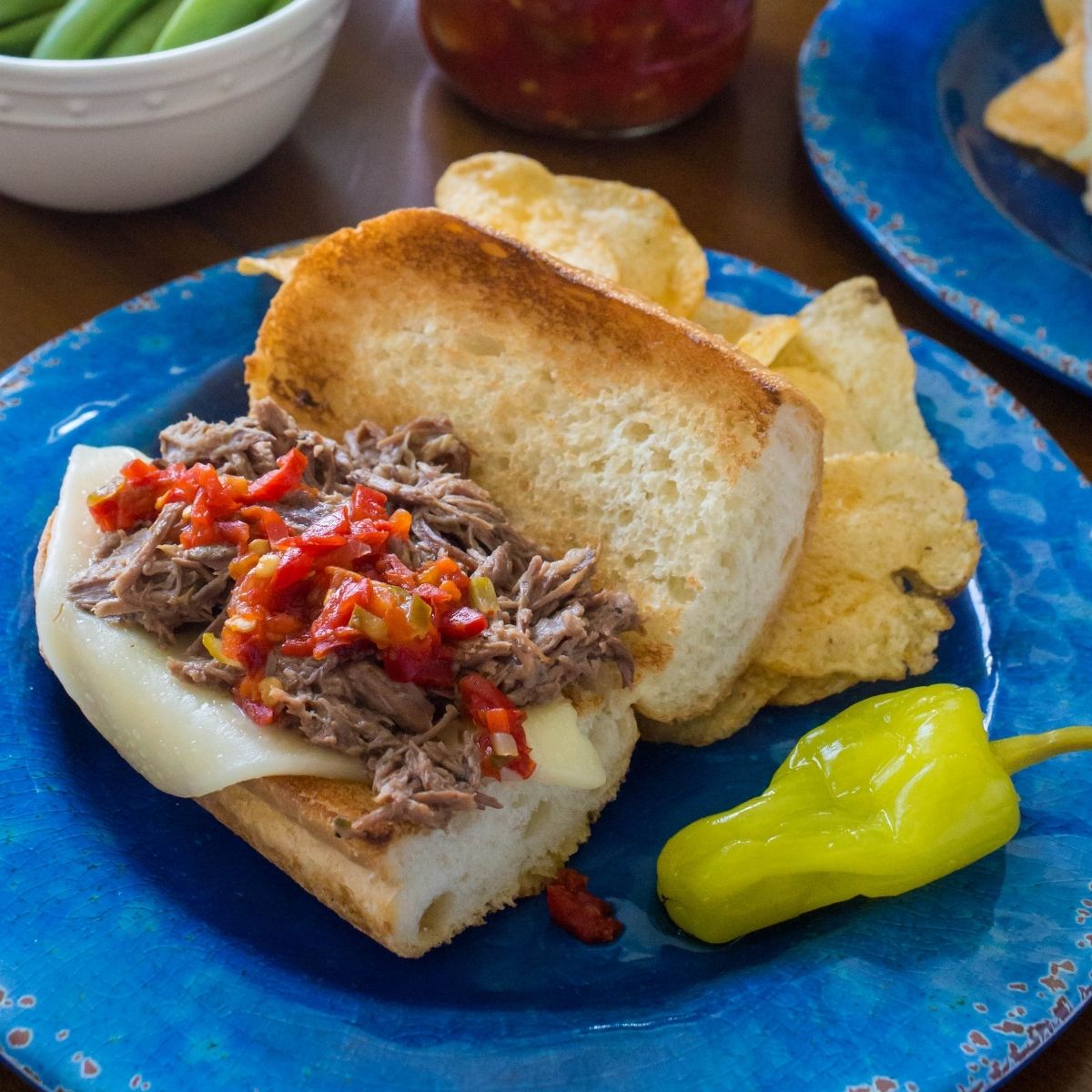 Italian beef sandwich has toasted bread, melted provolone cheese, and pepper relish on top of the shredded beef.