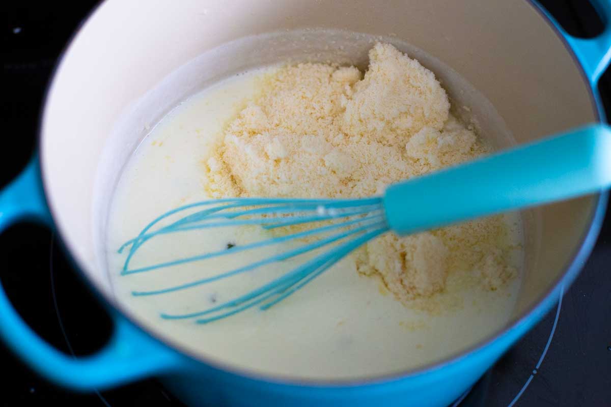 The finished alfredo sauce has a whisk mixing in the grated parmesan cheese.