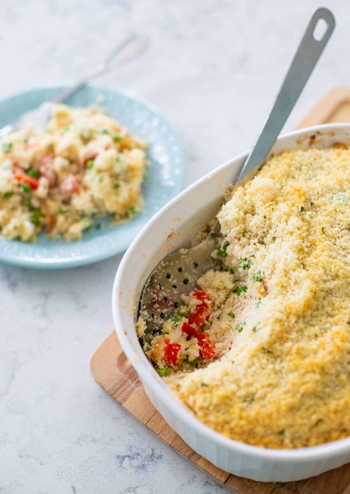 The baked casserole has a serving spoon scooping out a portion onto a blue plate.