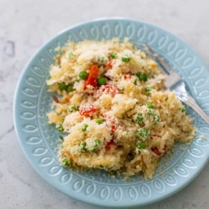 A blue plate has a serving of chicken rice alfredo casserole. You can see the red peppers and peas popping up through out the serving.
