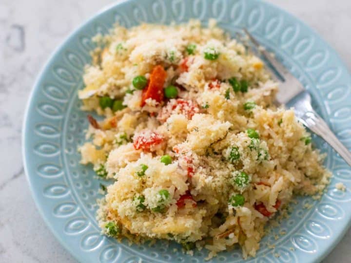 A blue plate has a serving of chicken rice alfredo casserole. You can see the red peppers and peas popping up through out the serving.