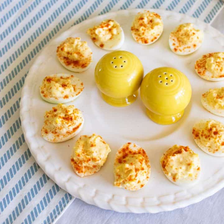 A platter of deviled eggs has a yellow salt and pepper shaker in the center.