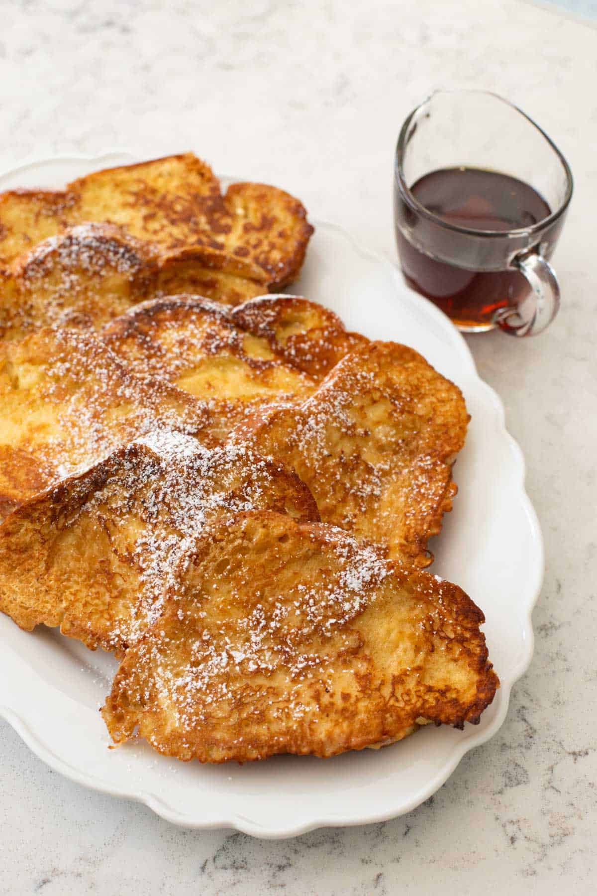 The finished french toast is served on a large white platter for the table. Maple syrup is on the side.