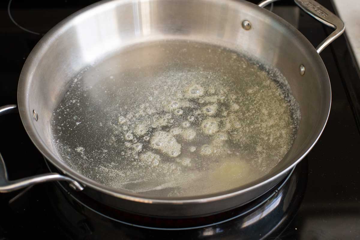 A non-stick skillet has melted butter that has begun to bubble.