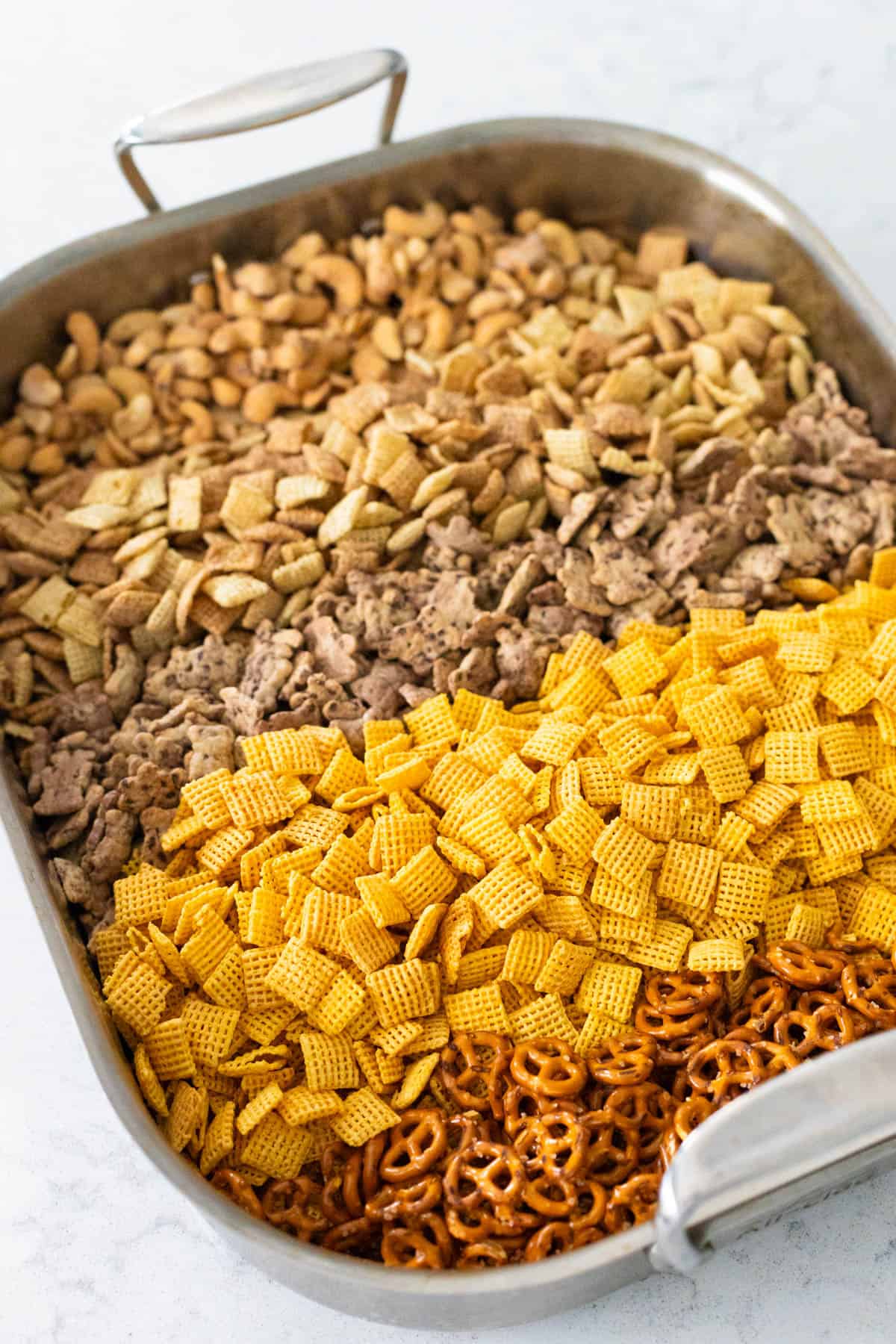 The roasting pan has the cereals, pretzels, and nuts ready for mixing.