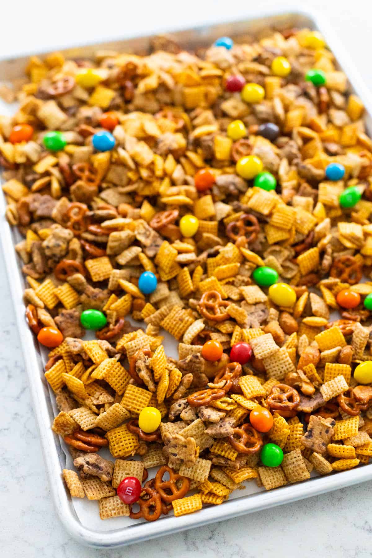 The M&M candies have been added to the cooled Chex mix on a baking sheet.