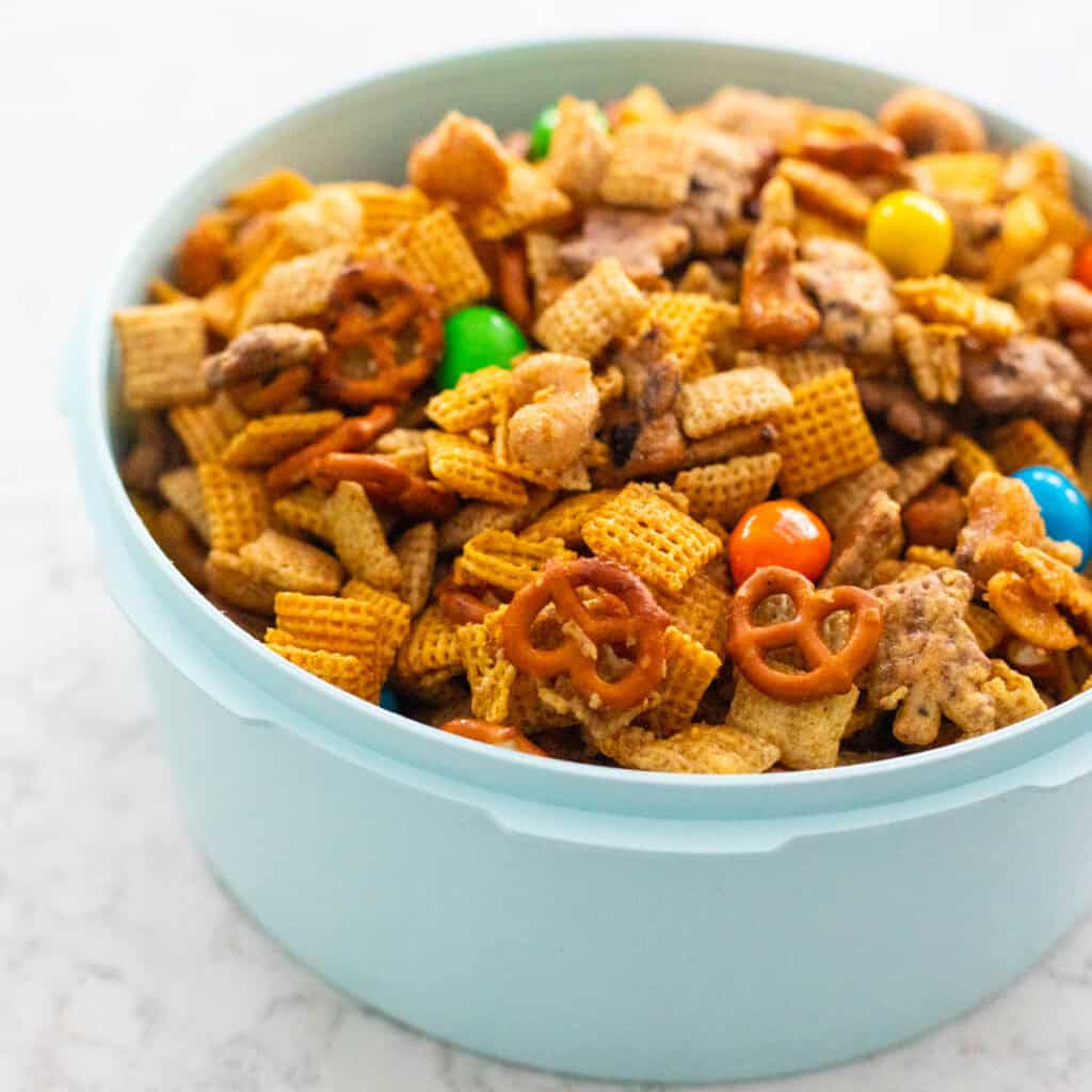 A blue bowl is filled with homemade Chex Mix with cereal, pretzels, M&Ms candies, and chocolate chip teddy grahams.