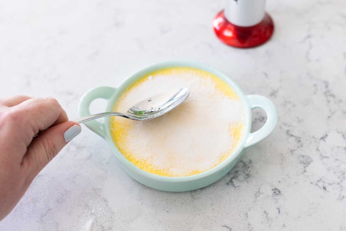 The sugar is being leveled out with the back of a spoon.