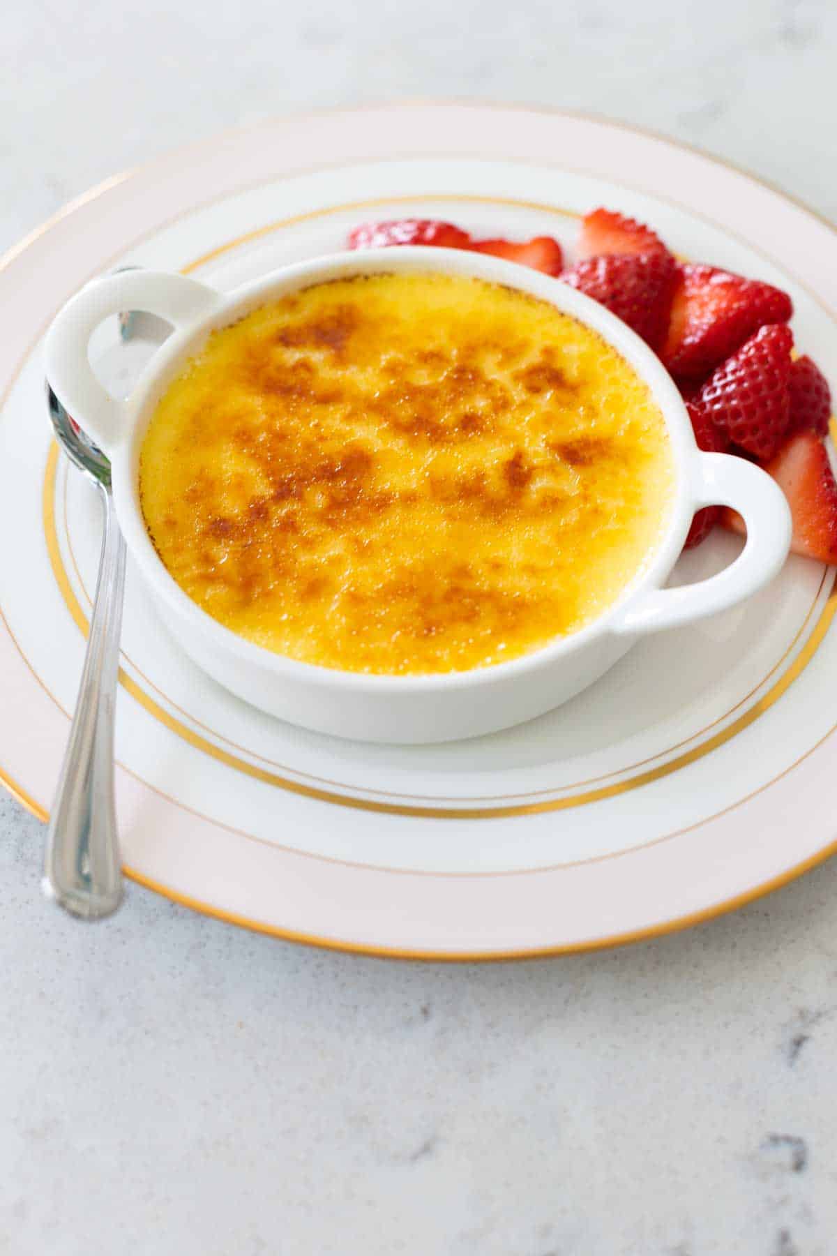 The finished custard dessert sits on a pink china plate with fresh strawberries and a spoon.