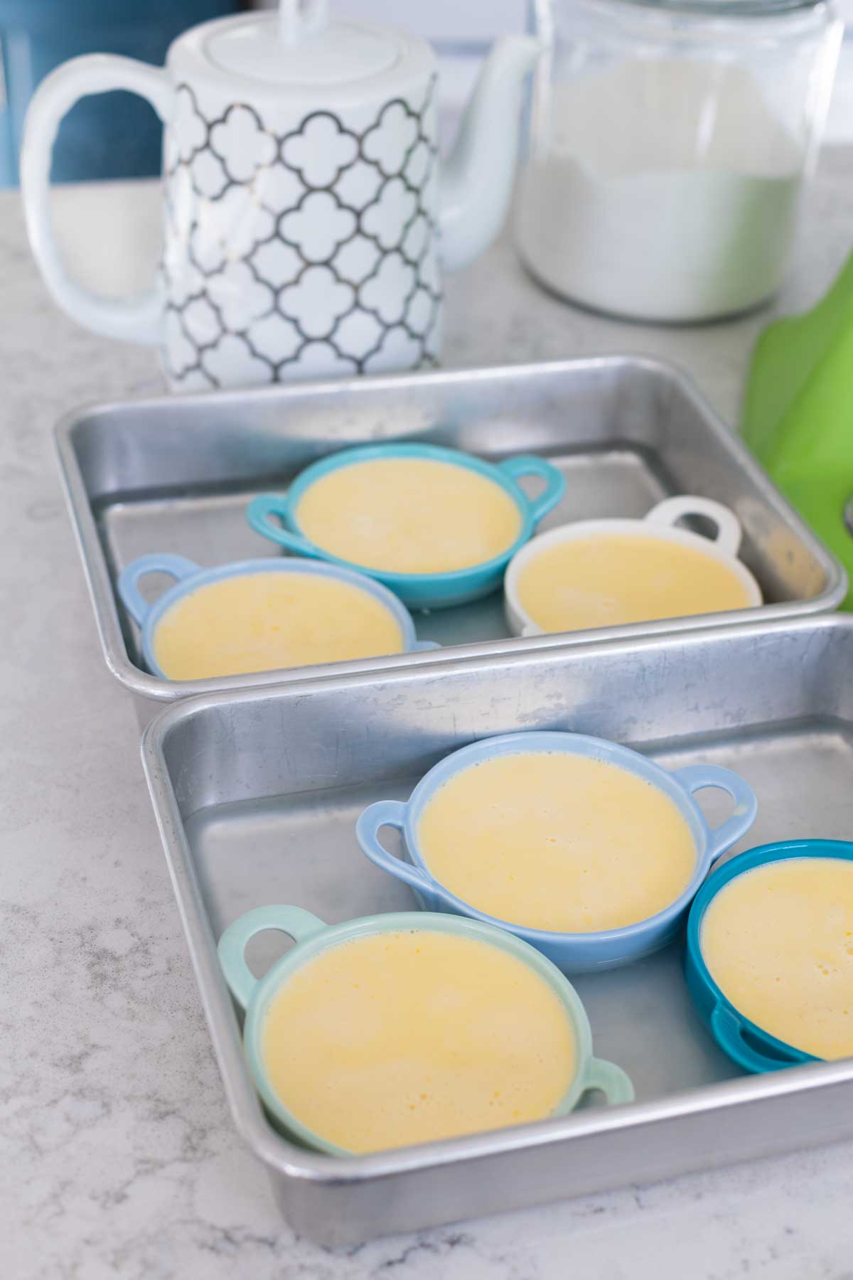 The filled ramekins are in the baking pans, a hot kettle of water is about to pour in the water for the water bath.