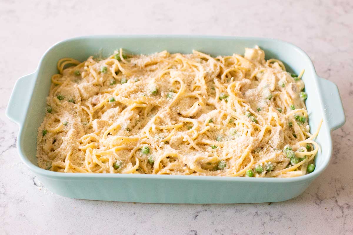 The chicken tetrazzini has been spread out in the blue baking dish and topped with grated parmesan cheese.