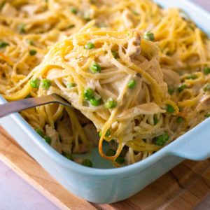 A blue baking dish has a spoon scooping out a serving of chicken tetrazzini pasta with peas.