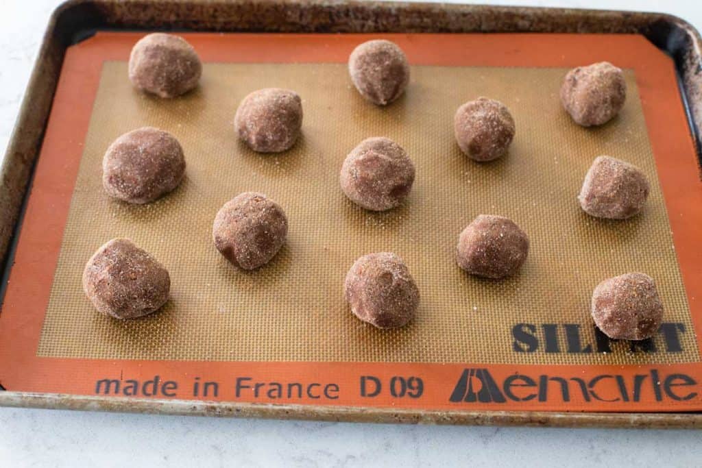 A cookie sheet is lined with a Silpat silicone mat and balls of cookie dough are lined up for baking.