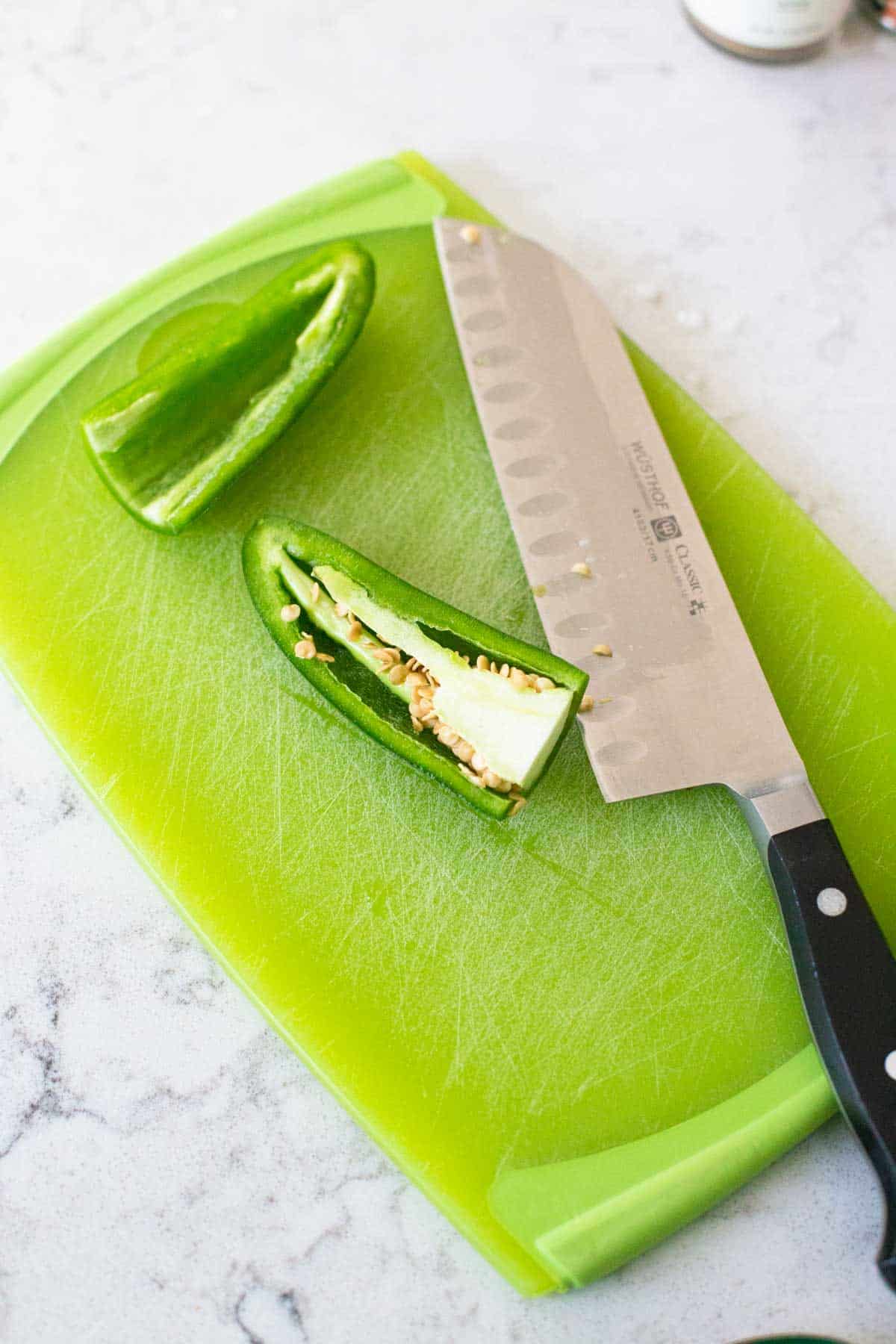 A fresh jalapeno pepper has been sliced in half and the seeds and ribs removed from one side.