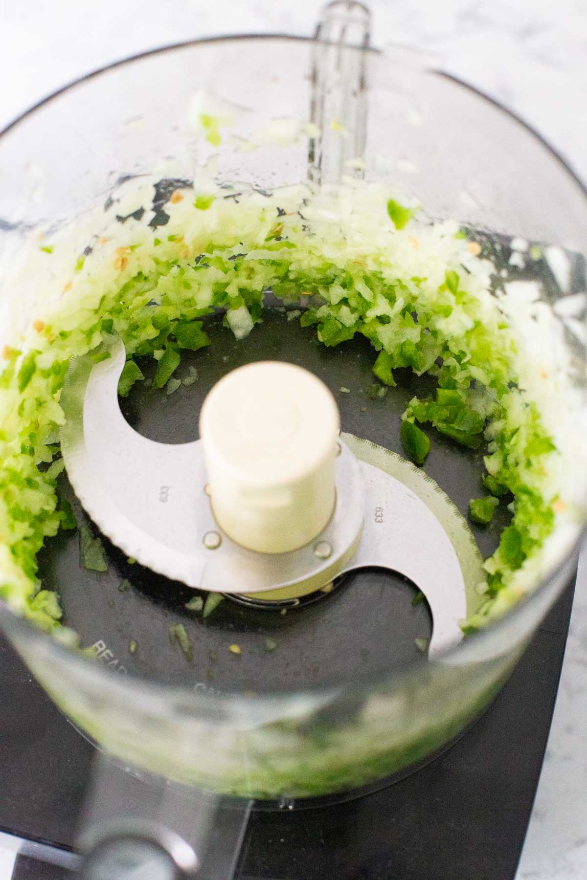 The fresh onion and jalapeno have been chopped in the bowl of a food processor with the blade attachement.