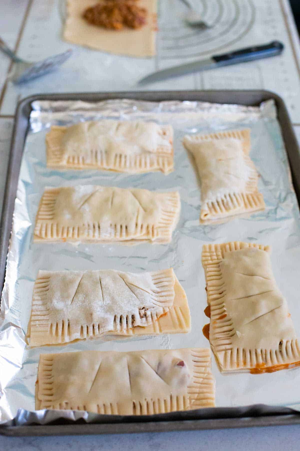 A baking sheet lined with foil has hand pies lined up for baking.