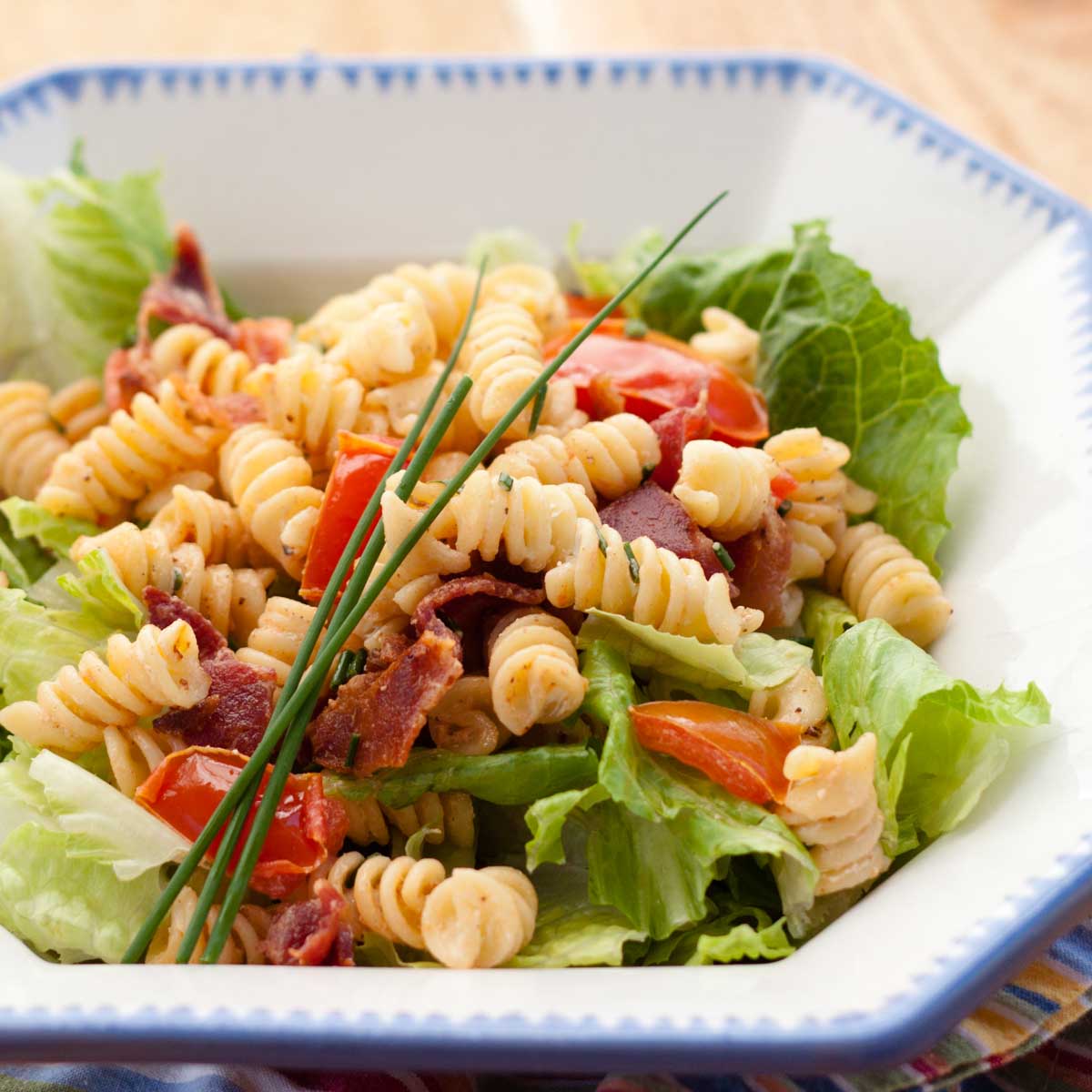 BLT pasta salad has corkscrew noodles, fresh lettuce, bacon, tomatoes, and fresh chives on top.