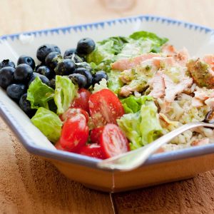 A big salad bowl shows the flaked leftover salmon, fresh blueberries, halved tomatoes, and green lettuce leaves.