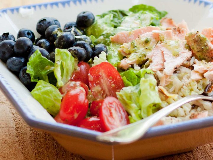 A big salad bowl shows the flaked leftover salmon, fresh blueberries, halved tomatoes, and green lettuce leaves.