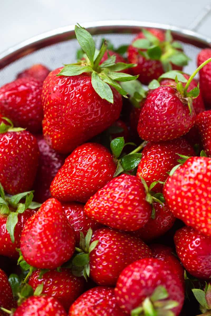 A bowl of fresh strawberries with green leafy tops.