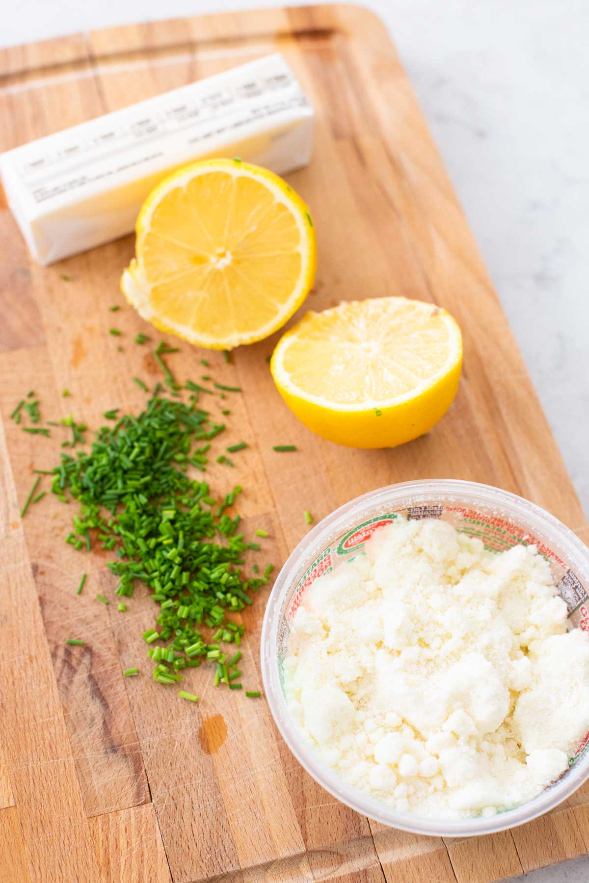 The fresh lemon, grated cheese, and fresh chives are on a cutting board with a stick of butter.