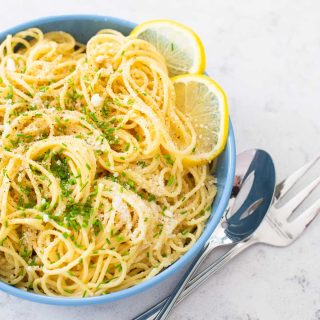 A bowl of spaghetti in a lemon butter sauce has fresh chives and slices of fresh lemon on the side.