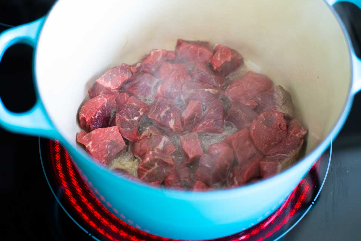 The chunks of beef are being browned in oil in a dutch oven on the stove top.