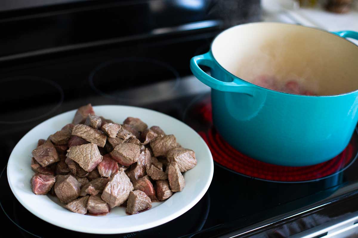 A dinner plate holds already browned stew meat while another batch cooks in the soup pot.