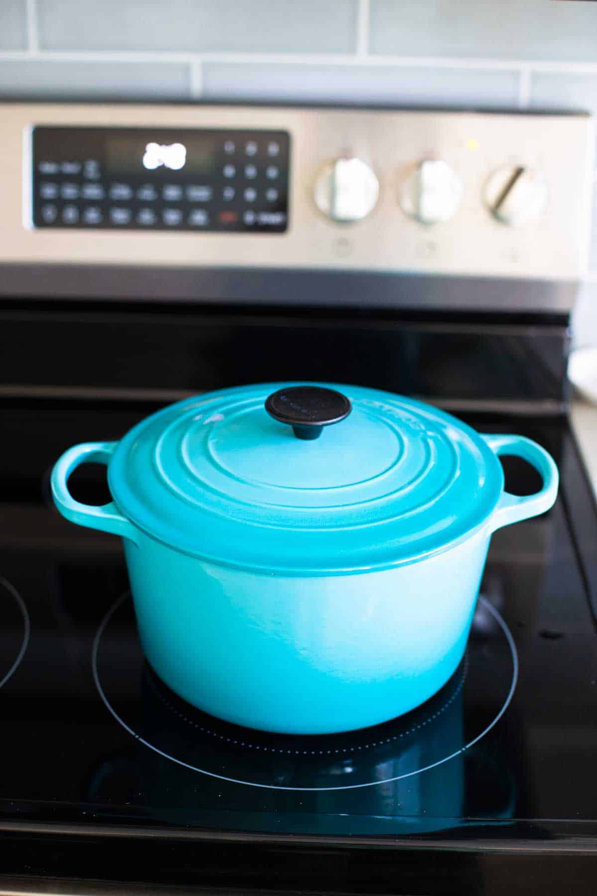 The blue dutch oven has the lid covering the stew cooking on the stove top.