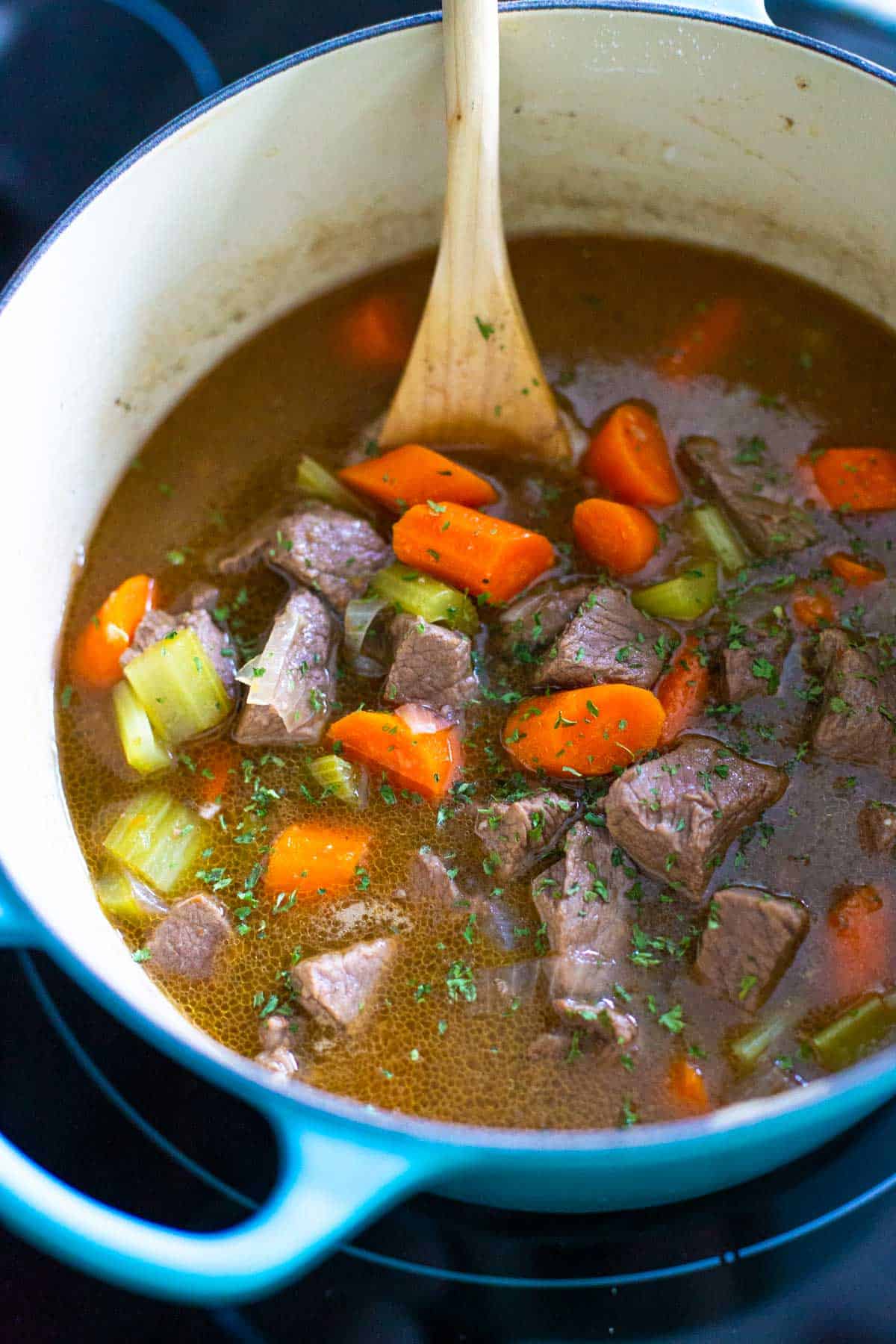 The finished beef stew sits in a dutch oven on the stove top.