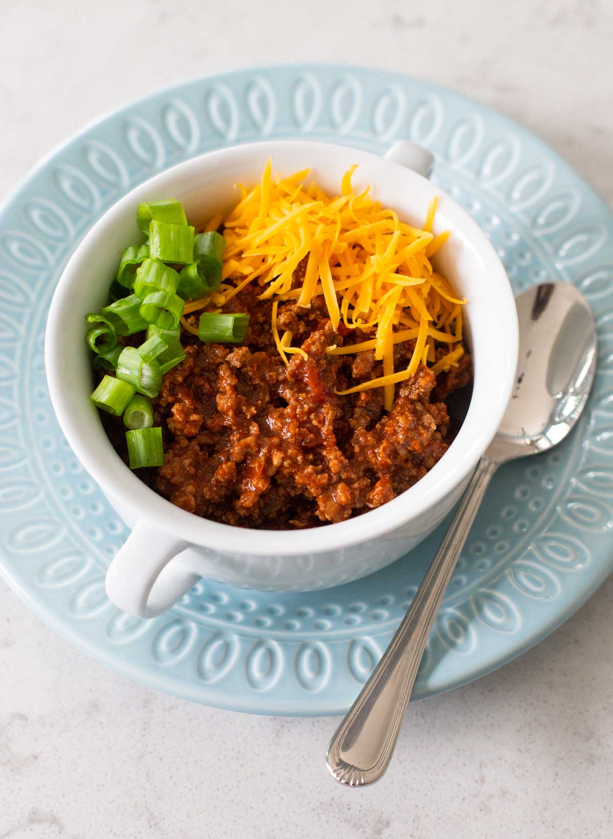 A bowl of ground beef chili is topped with cheddar cheese and green onions.