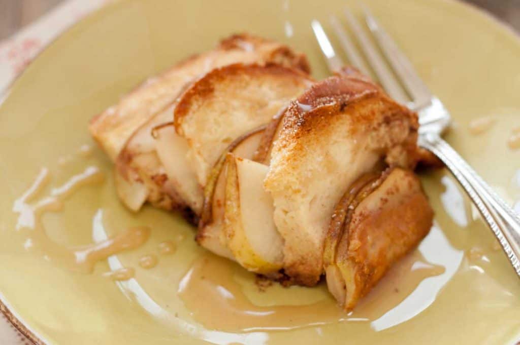 A close-up view of a serving of bread pudding with sliced pears and chocolate. There's a drizzle of caramel sauce over the top.