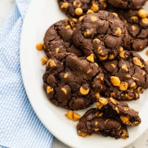 A white platter is filled with chocolate cookies with peanut butter chips scattered about.