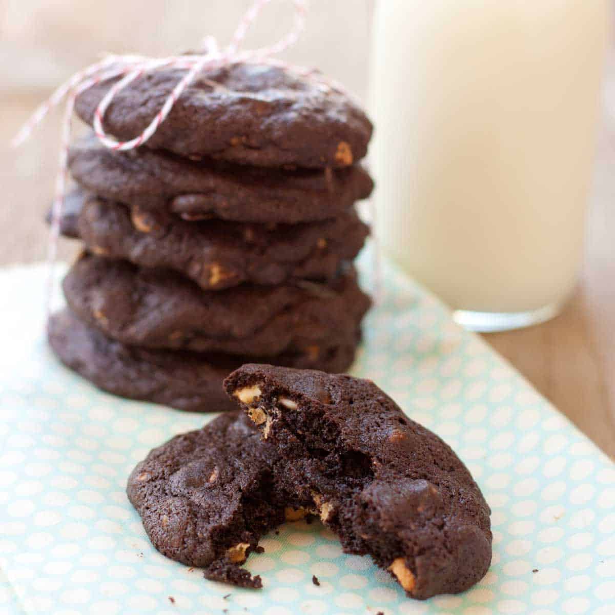 A stack of chocolate peanut butter chip cookies with one cookie in the front broken in half to show the inside.