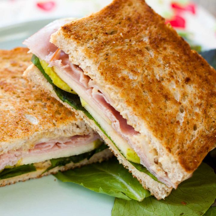 A grilled ham, pear, and havarti sandwich is cut in half so you can see the layers of filling inside.