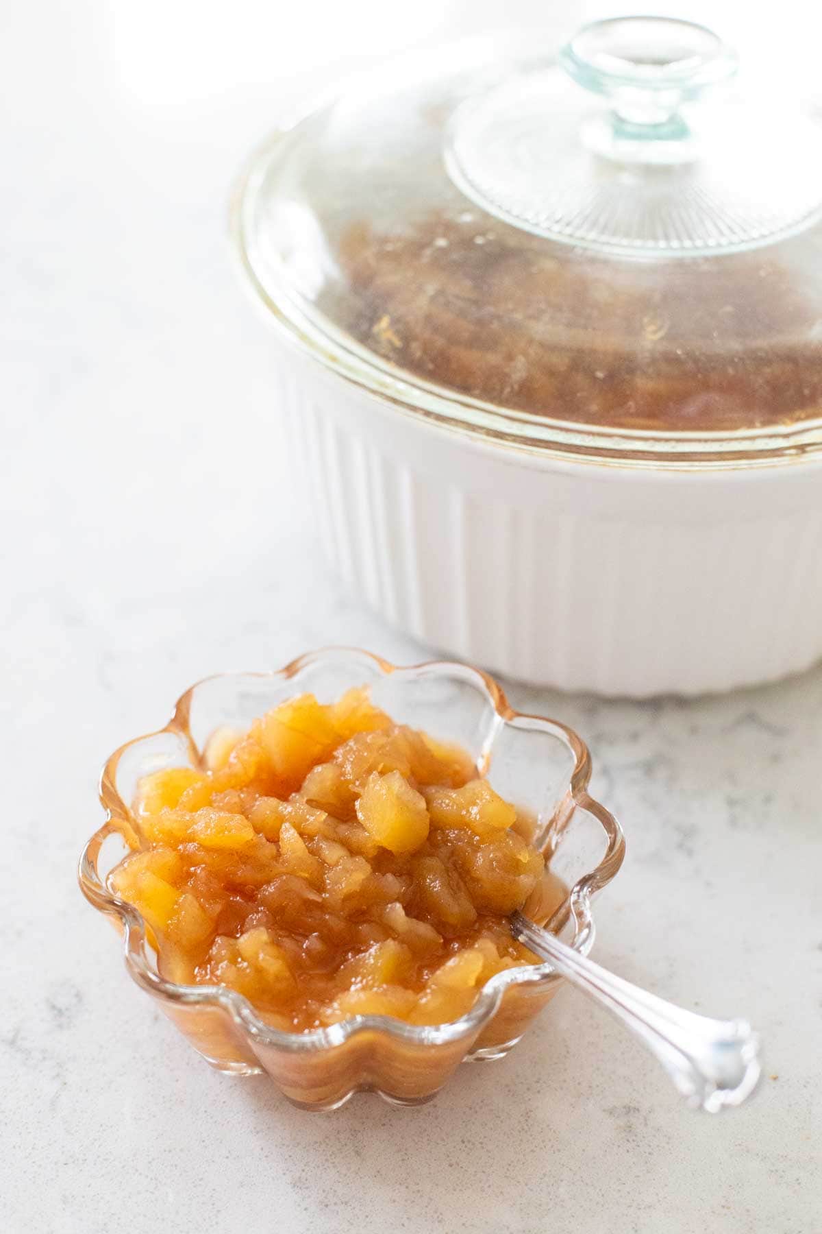 The microwave container sits behind a serving of cinnamon applesauce with a spoon.