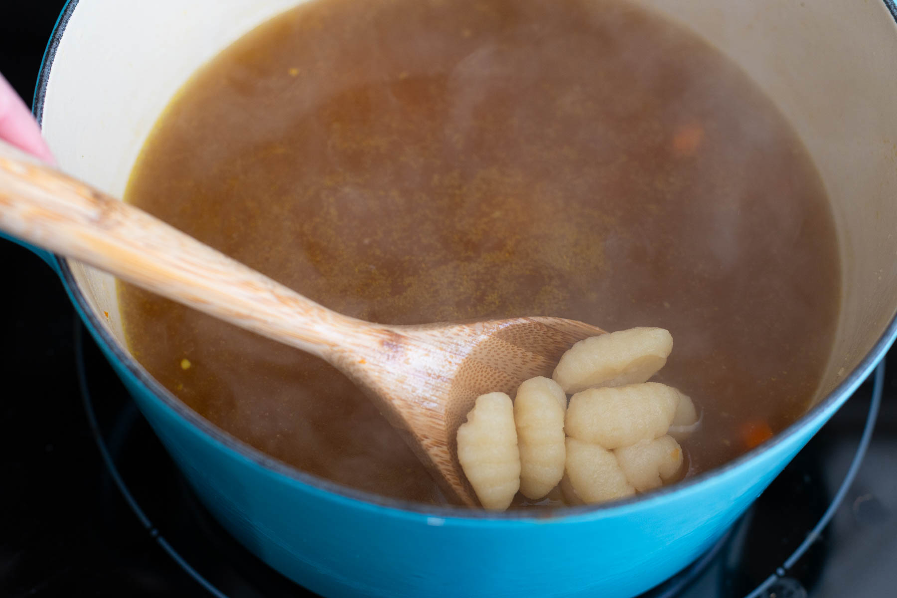 The gnocchi have been added to the soup but are so heavy they sink to the bottom. A spoon pulls some to the surface so you can see they are in the pot.