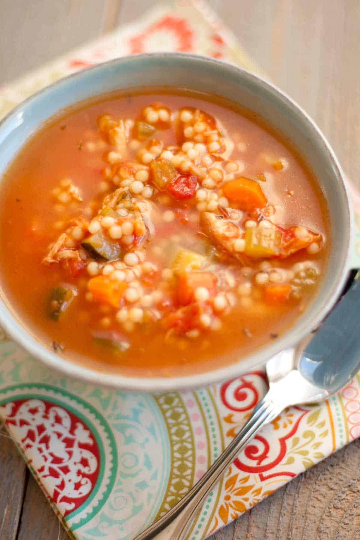 A bowl of Tuscan chicken soup with round noodles, tomato broth, and fresh veggies chopped up inside.