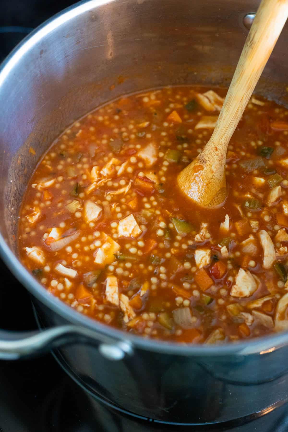 The finished soup is being stirred by a wooden spoon in a large soup pot.