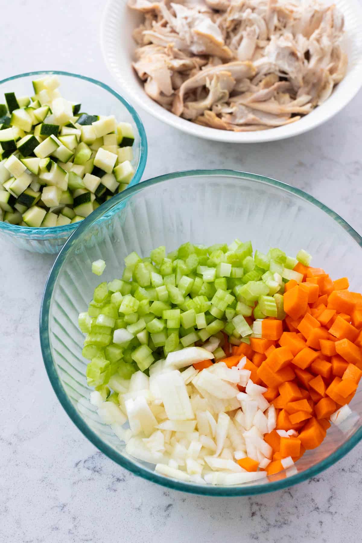 The onion, carrot, celery, and zucchini have been small diced and the rotisserie chicken is shredded in a bowl.