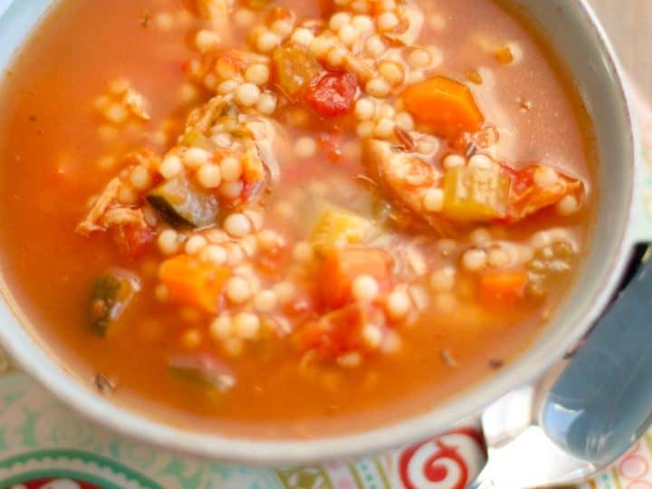 A bowl of Tuscan chicken soup with round noodles, tomato broth, and fresh veggies chopped up inside.