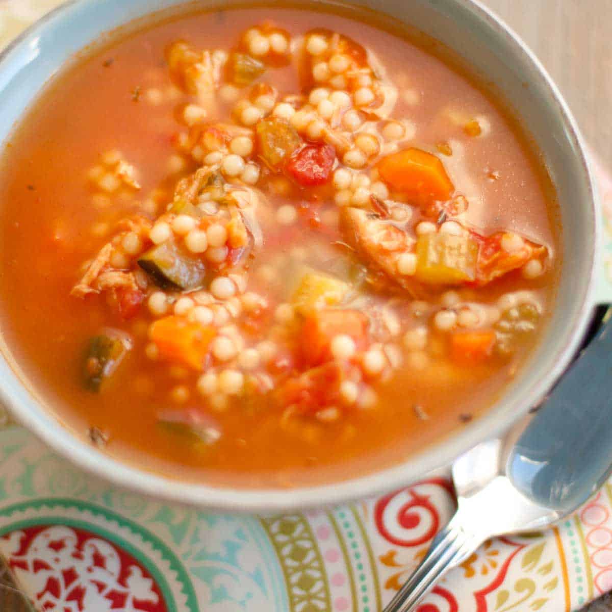 A bowl of Tuscan chicken soup with round noodles, tomato broth, and fresh veggies chopped up inside.