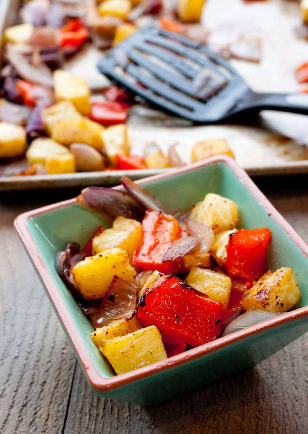 A small square dish has a serving of the roasted peppers sitting in front of the baking sheet with a spatula.