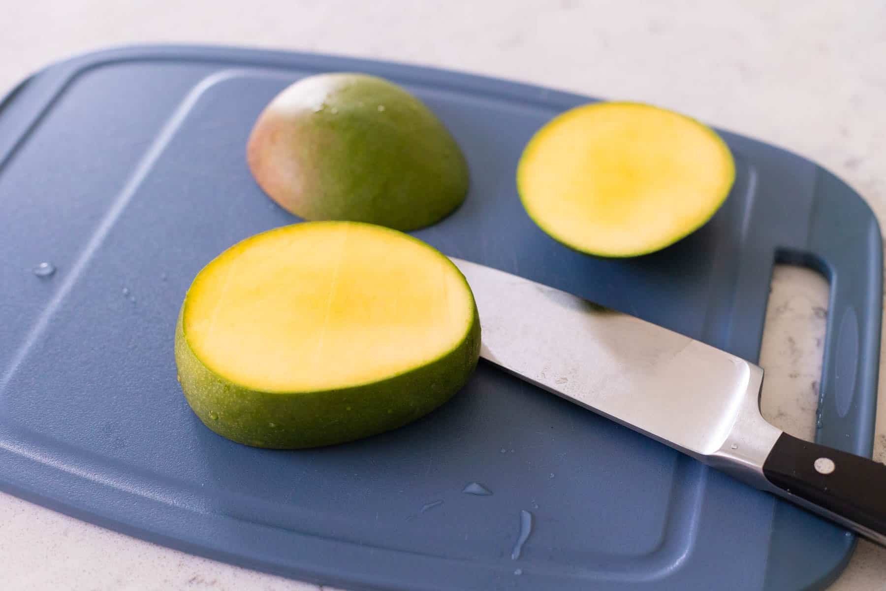 The fresh mango has been sliced into thirds on a cutting board.