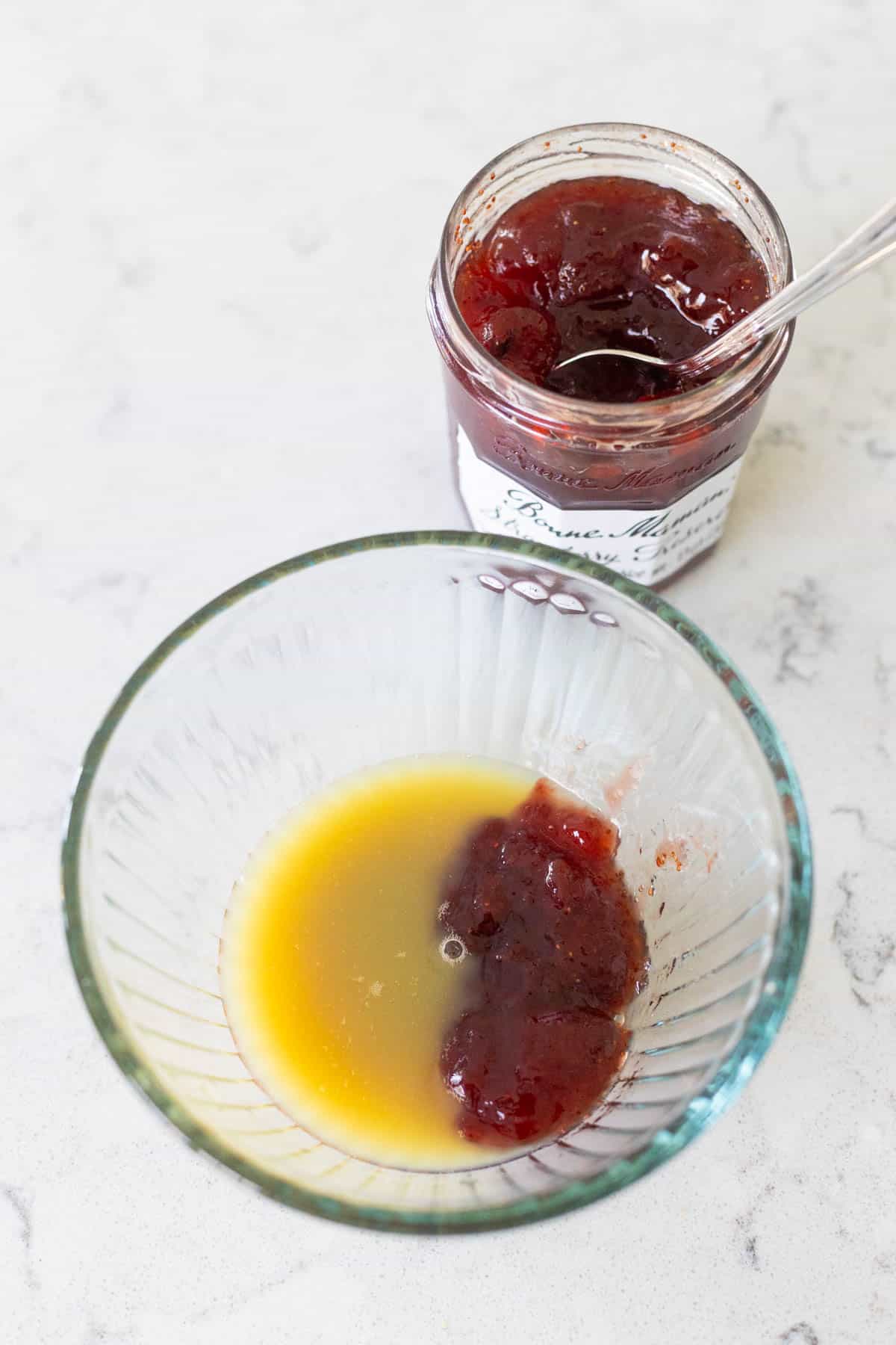 The jar of strawberry jam is next to the bowl filled with orange juice.