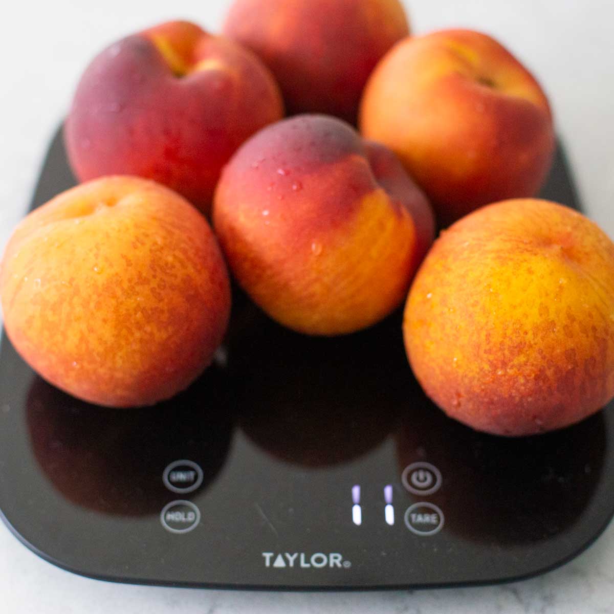A pile of fresh peaches sit on a food scale.