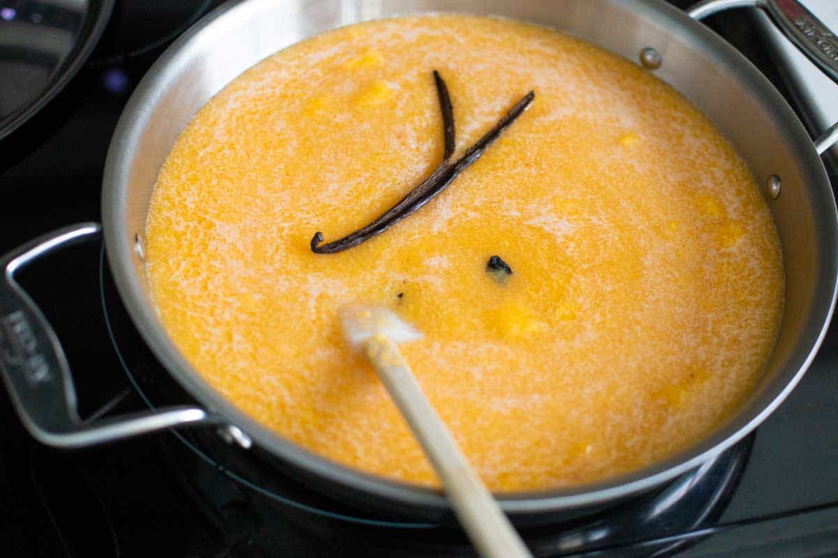 A vanilla bean pod floats in the peach jam in a large skillet.